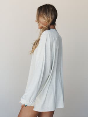 A relaxed, oversized long sleeve tee in a soft stripe shoots from a side-back angle — the kind of top that looks equally at home on a Sunday morning or tucked into cutoffs for a casual afternoon out.
