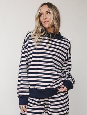 A relaxed striped sweatshirt in navy, cream, and red worn as a matching set — effortlessly casual with gold layered necklaces and stacked rings giving it just enough personality.