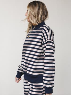 A side-profile shot of a model in a matching navy striped sweatshirt and pants set — relaxed, effortlessly cool, with a gold chain necklace and stacked rings adding just enough personality.