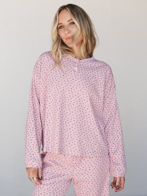 A relaxed long-sleeve henley top in soft pink with an all-over ditsy floral print, styled as a matching set with coordinating pants — the kind of outfit that makes staying in feel intentional.