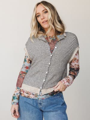 A layered look that does the mixing-and-matching work for you — a striped knit sweater vest buttons over a floral long-sleeve top, worn with wide-leg denim for that effortlessly collected, I-just-threw-this-on energy.