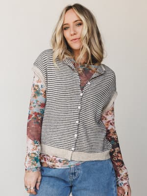 A relaxed, layered look built around a striped sweater vest worn over a floral long-sleeve top and finished with light-wash jeans — the kind of effortless mix-and-match that looks like it came together without trying.