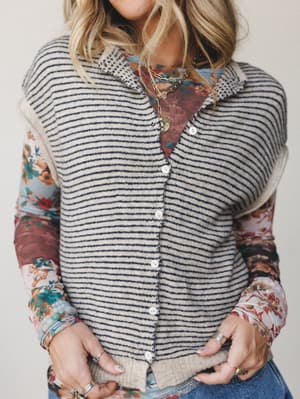 A striped knit sweater vest layered over a mixed floral print long-sleeve top, styled with stacked gold and silver jewelry — the kind of effortless, lived-in combo that looks like you meant to do it.