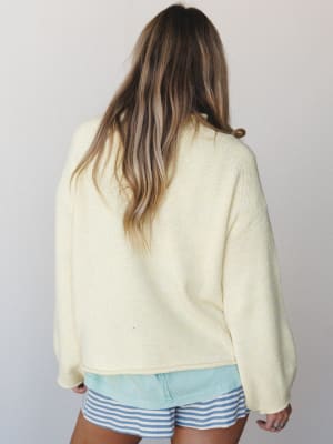 A back-facing shot of a soft butter-yellow knit sweater paired with blue and white striped shorts — the kind of easy, sun-warmed combination that feels like the last day of a beach trip.