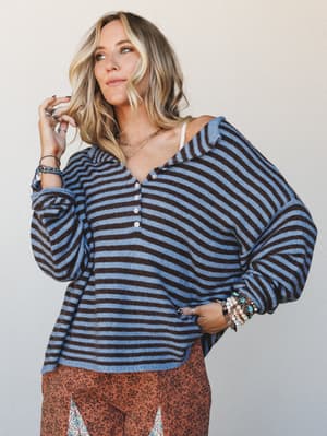 A relaxed striped henley top styled with stacked boho jewelry and a floral skirt peeking out at the hem — the kind of effortless outfit that looks like you thought about it just enough.