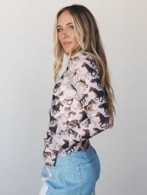 A model shot in profile wearing a long-sleeve horse-print top in dusty rose paired with light wash jeans — the kind of laid-back, expressive outfit that looks like it was put together effortlessly but definitely wasn't an accident.