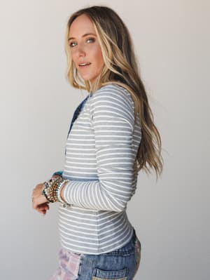 A side-profile shot of a model in a fitted heather gray striped long-sleeve top layered over a printed piece, stacked with colorful beaded bracelets — relaxed and put-together in the best way.