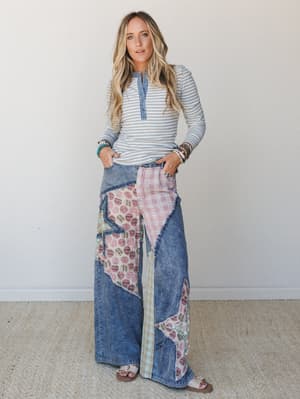 A relaxed full-body shot of a model in a striped henley long-sleeve paired with statement wide-leg patchwork jeans — the kind of outfit that looks effortless but has clearly been thought about.