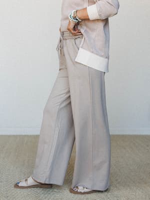 A relaxed, tonal set styled with easy confidence — wide-leg sweatpants in a soft ash mocha pair with a matching top featuring contrast cream cuffs, stacked beaded bracelets, and slide sandals for an effortlessly put-together everyday look.