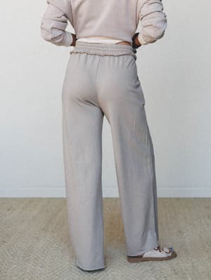 Shot from behind, a model in wide-leg sweatpants and a cropped sweatshirt pairs the soft, relaxed set with sandals — the kind of outfit that makes doing nothing feel very intentional.