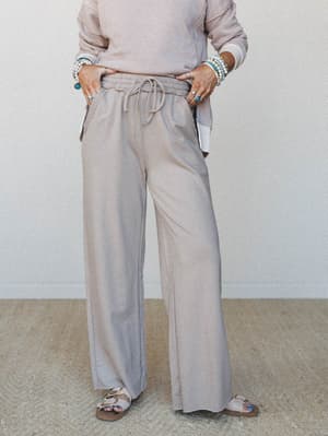 Wide-leg sweatpants in a soft ash mocha tone styled with a matching pullover, sandals, and stacked turquoise and pearl bracelets — the kind of outfit that looks intentional even when you're taking it easy.