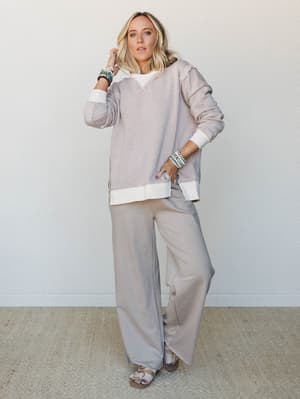 A relaxed, tonal set in soft ash mocha — an oversized sweatshirt with cream contrast banding paired with wide-leg sweatpants and layered bead bracelets, the kind of outfit that makes staying home feel completely intentional.