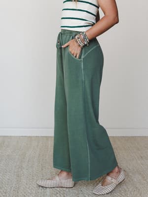 A side-profile shot of wide-leg drawstring pants in a washed army green, styled with a striped crop top, stacked beaded bracelets, and woven flats — the kind of outfit that looks effortless but was absolutely thought about.