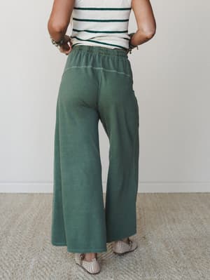 Back view of wide-leg army green pants with a relaxed, lived-in wash, styled with a cream striped top and woven flats — easy, earthy, and the kind of outfit that looks effortless on purpose.