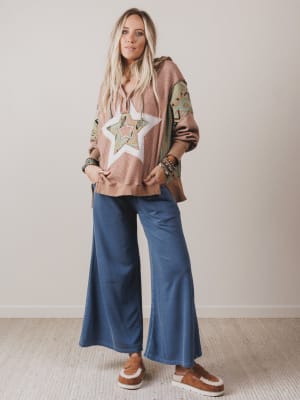 Woman wearing a star-patterned top and blue pants against a plain background