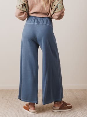 Person wearing blue wide-leg pants and a patterned top against a neutral background