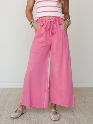 Wide-leg fuchsia drawstring pants in a soft, washed fleece fabric styled with a striped crop top and woven flats — the kind of outfit that looks like you tried just enough.