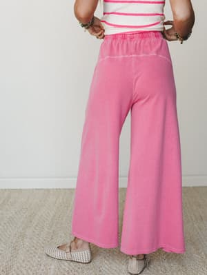 A back-view shot of wide-leg fuchsia sweatpants with a ruched elastic waistband, styled with a striped crop top and woven flats — effortless and a little playful, like she's running errands but make it intentional.