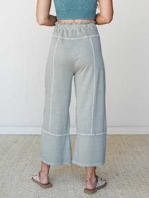A back-view shot of wide-leg cropped pants in a washed sage green, styled with a teal textured crop top and neutral sandals — relaxed and put-together in the best way.