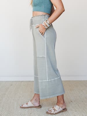 A side-profile shot of wide-leg lounge pants in a washed sage tone, styled with a matching textured crop top, layered bead bracelets, and buckle sandals — relaxed and put-together at the same time.