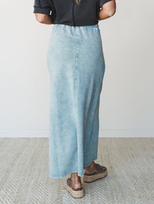 Shot from behind, a model styles a washed ash blue maxi skirt with a charcoal waffle knit top and leopard print espadrille flatforms — the kind of effortless, lived-in outfit you'd actually reach for on a slow Saturday.