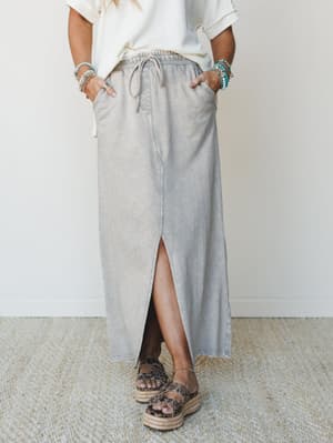 A washed gray maxi skirt with a relaxed drawstring waist and front slit is styled with a cream waffle knit top, platform espadrille sandals, and layered turquoise and beaded bracelets — easy, lived-in boho for everyday.