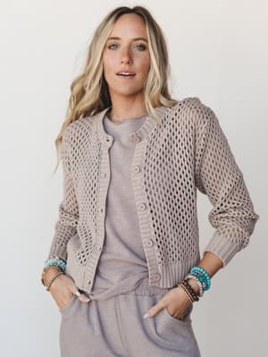 An open-knit button-front cardigan in warm ash mocha layered over a matching relaxed tee and joggers, styled with stacked beaded bracelets — the kind of effortless tonal look that feels pulled together without trying.