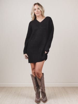 Woman wearing a black sweater dress and brown cowboy boots against a plain background