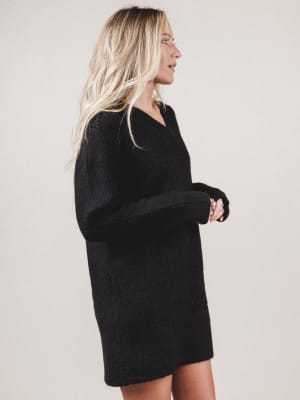 Woman wearing a black sweater dress against a plain background