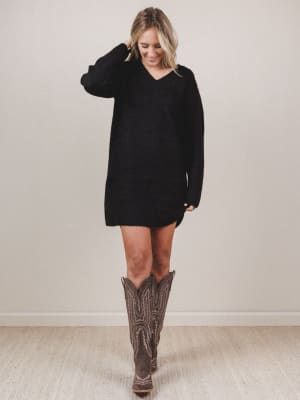 Woman wearing a black sweater dress and brown knee-high boots on a plain background