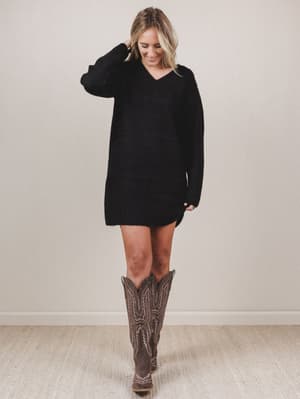 Woman wearing a black sweater dress and brown knee-high boots on a plain background