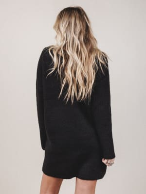 Person wearing a black sweater dress with long blonde hair on a plain background