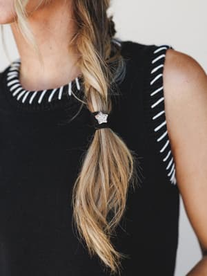 A close-up lifestyle shot highlighting a rhinestone star hair tie against a loose braid, styled over a black sweater tank with white stripe knit trim detailing — effortless and a little sparkly.