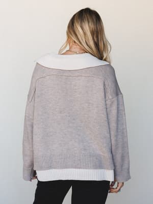 Shot from behind, this oversized knit sweater in warm heathered mocha layers over a white ribbed underlayer, giving it that effortlessly put-together look — the kind of outfit that feels cozy but still looks like you tried.