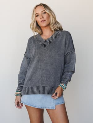 An oversized acid-wash charcoal knit sweater styled over a denim mini skirt, layered with stacked turquoise and beaded bracelets — the kind of effortless combo that looks like it came together in three minutes but somehow just works.