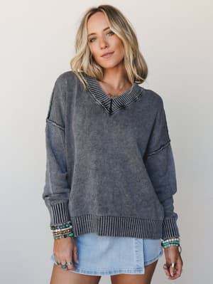 An oversized acid-wash knit sweater in faded charcoal is layered over a light denim mini skirt, styled with stacks of turquoise and mixed-metal bracelets — the kind of effortless outfit that looks like it came together without trying.