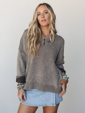 An oversized knit sweater in washed brown styled over a light denim mini skirt, layered with stacks of turquoise and mixed-metal bracelets — the kind of effortless combo that looks like it came together in five minutes but took a lot of practice.
