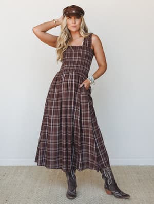 A smocked brown plaid midi dress with a full tiered skirt, styled with cowboy boots and a leather newsboy cap for a Western-boho look that feels like fall came early and brought good energy with it.