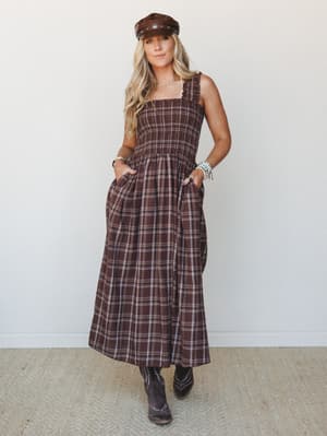 A smocked plaid midi dress in deep brown styled with cowboy boots and a leather newsboy cap — the kind of outfit that looks equally at home at a fall farmers market or a country concert.