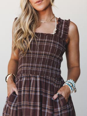 A smocked brown plaid dress styled with layered gold necklaces, beaded bracelets, and gold bangles — the kind of outfit that feels intentional without trying too hard, equally at home on a fall farmers market run or a weekend brunch.