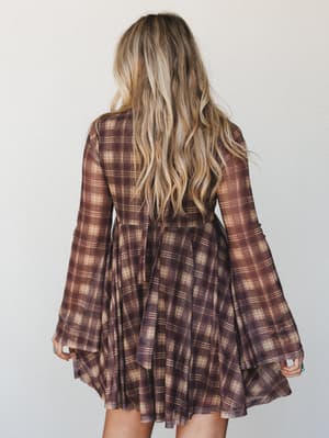 A flowy plaid mini dress shot from behind, its dramatic bell sleeves and full skirt giving it that perfect mix of vintage energy and free-spirited ease — the kind of dress that looks good spinning in a field or walking into a fall farmers market.