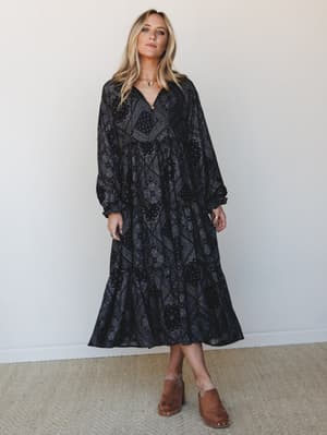A moody, effortlessly boho maxi dress in a deep black bandana print, styled with tan studded clogs and a gold choker — the kind of outfit that looks equally at home at a fall farmers market or a candlelit dinner.