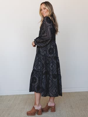 A tiered midi-maxi dress in a deep black bandana-paisley patchwork print, styled with tan suede platform clogs and a turquoise ring — the kind of outfit that feels effortless but clearly wasn't an accident.