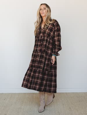 A plaid tiered maxi dress in deep brown and cream styled with tan cowboy boots and turquoise jewelry — the kind of fall outfit that feels intentional without trying too hard.