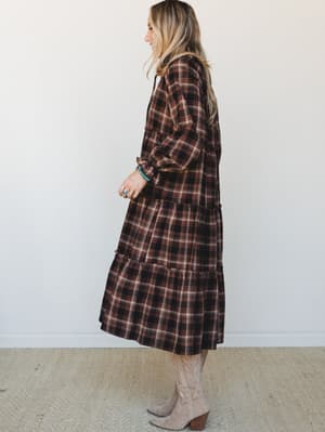 A tiered plaid midi dress in deep brown and black styled with tan cowboy boots and turquoise jewelry — the kind of fall outfit that feels cozy and intentional at the same time.