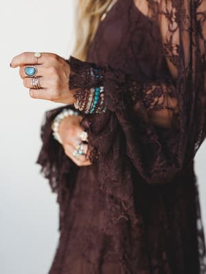 A close-up detail shot of a deep plum lace dress, hands stacked with turquoise and pearl jewelry — the kind of styling that feels genuinely collected, not coordinated.