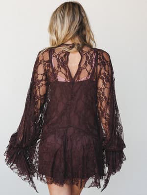 Shot from behind, this deep plum lace mini dress layers sheer floral lace over a slip-style underlayer, with dramatic bell sleeves that cascade into tiered ruffled cuffs — romantic and a little moody in the best way.