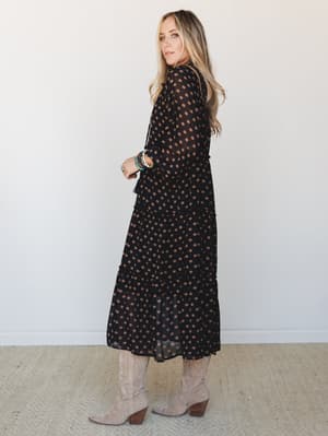 A flowy black midi dress with warm bronze floral dot print, styled with tall suede cowboy boots and stacked bracelets — the kind of outfit that works equally hard at a fall wedding and a Saturday farmers market.