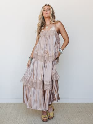 A flowy tiered maxi dress in a soft sand tie-dye with satin sheen and lace trim details, styled with turquoise jewelry and wooden platform sandals for a romantic, free-spirited feel.