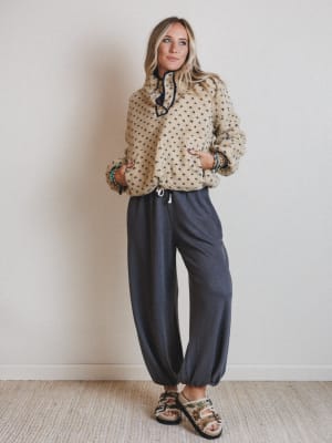 Woman wearing a beige patterned sweater and dark blue pants against a plain background